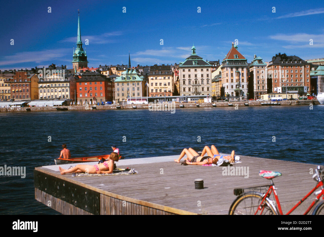 Sweden, Stockholm. Sunbathing On Skeppsholmen, With Skeppsbron And The Spire Of Tyska Kyrkan Behind. Stock Photo