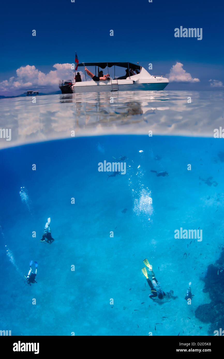 Scuba divers swimming under white dive boat on the ocean surface. Horizontal split over/under color image. Stock Photo