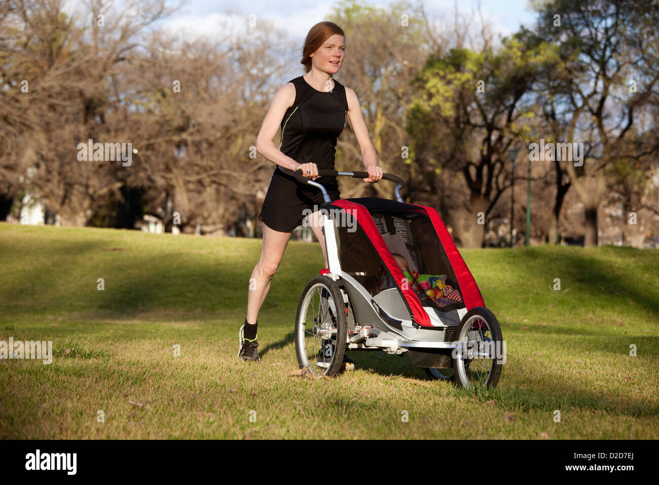 A woman jogging in a park and pushing a baby stroller Stock Photo