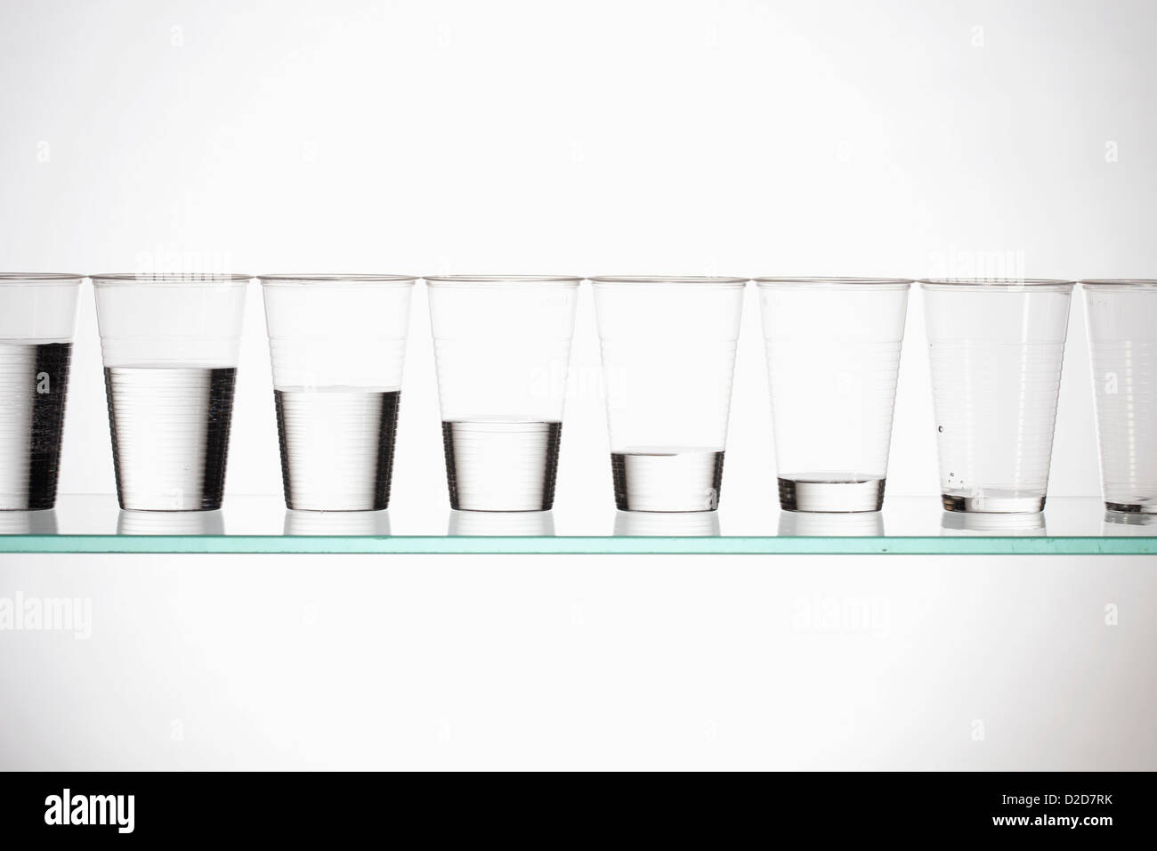 A row of glasses with varying amounts of water descending from full to empty Stock Photo