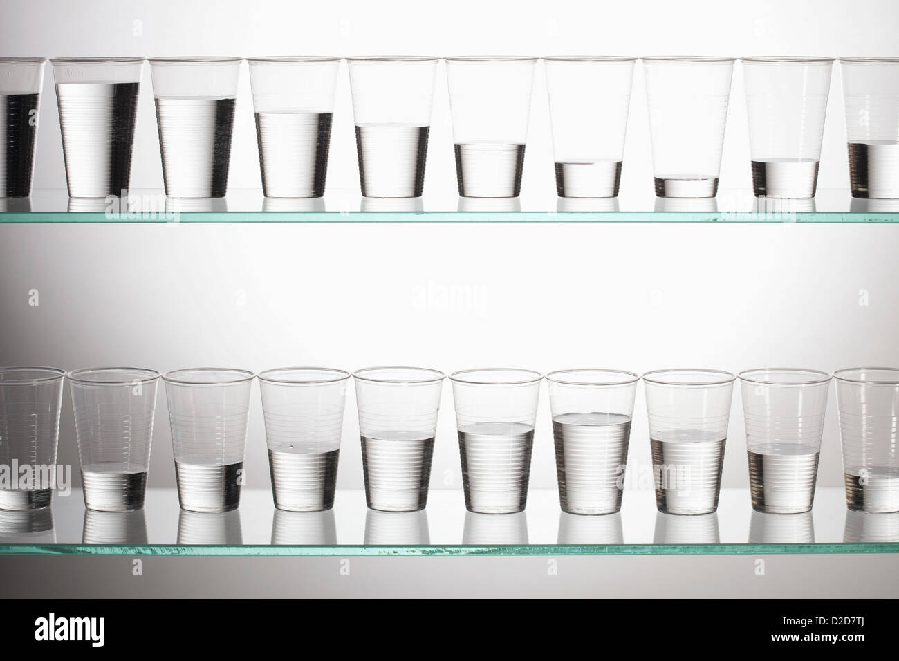 Two shelves with glasses of water filled with varying amounts of water Stock Photo