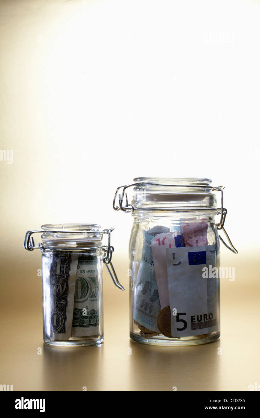 Dollar in a little jar beside larger jar full of euros Stock Photo