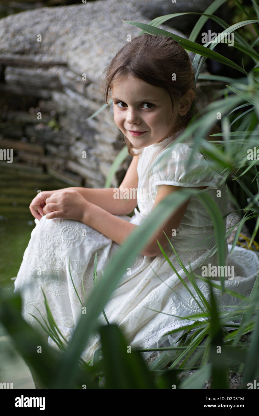 A young girl in a white dress sitting in nature Stock Photo