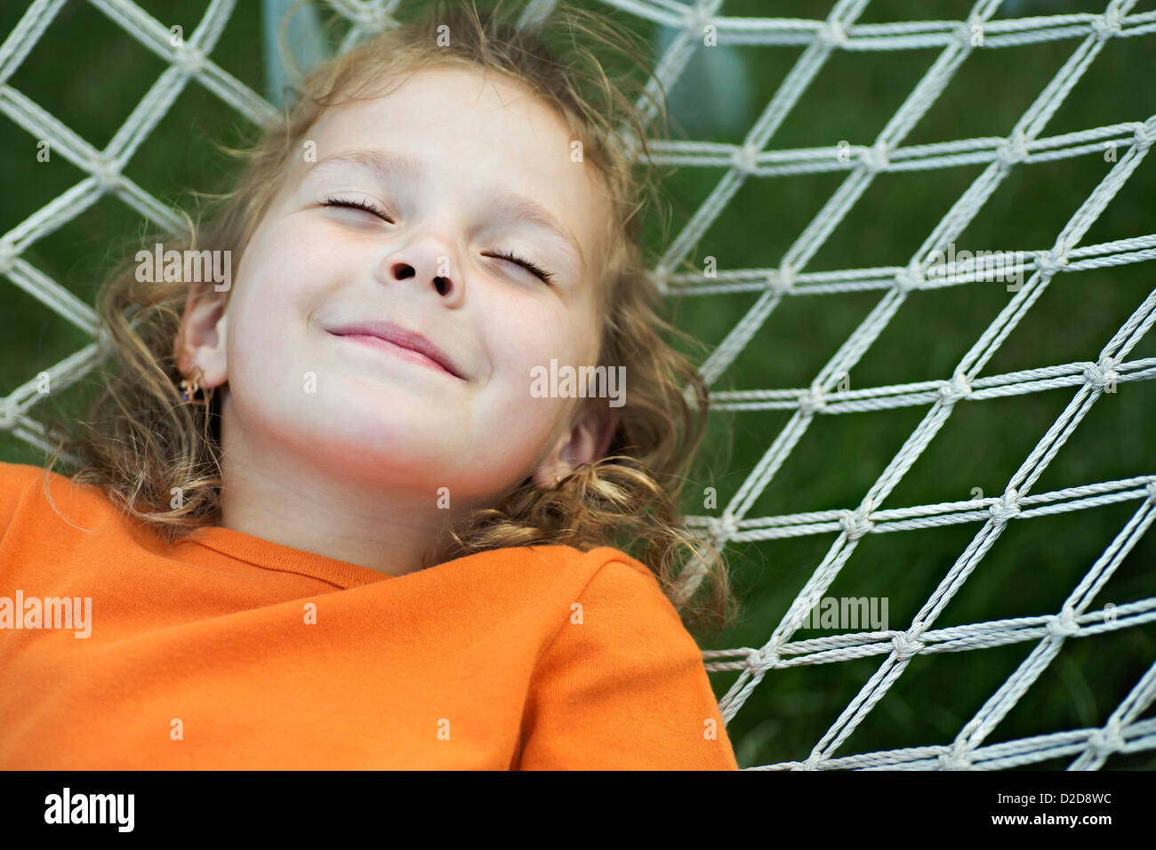 A young smiling girl lying on a hammock with her eyes closed Stock Photo