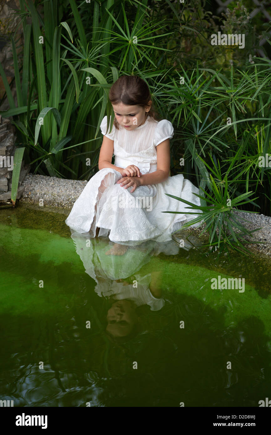 A young girl looking curiously into pond water Stock Photo