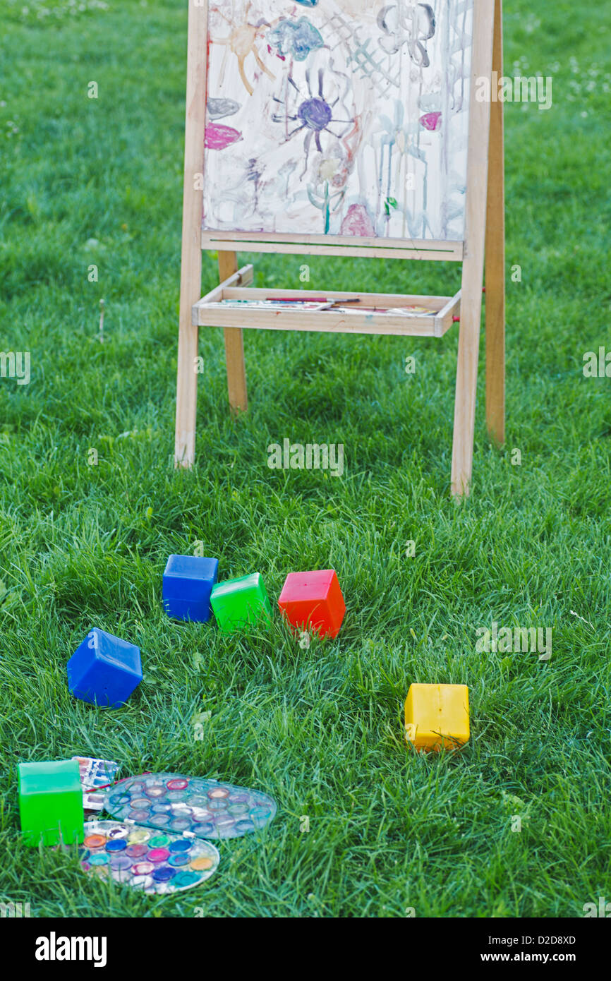 An easel, toy blocks and watercolor paints in the grass of a backyard Stock Photo