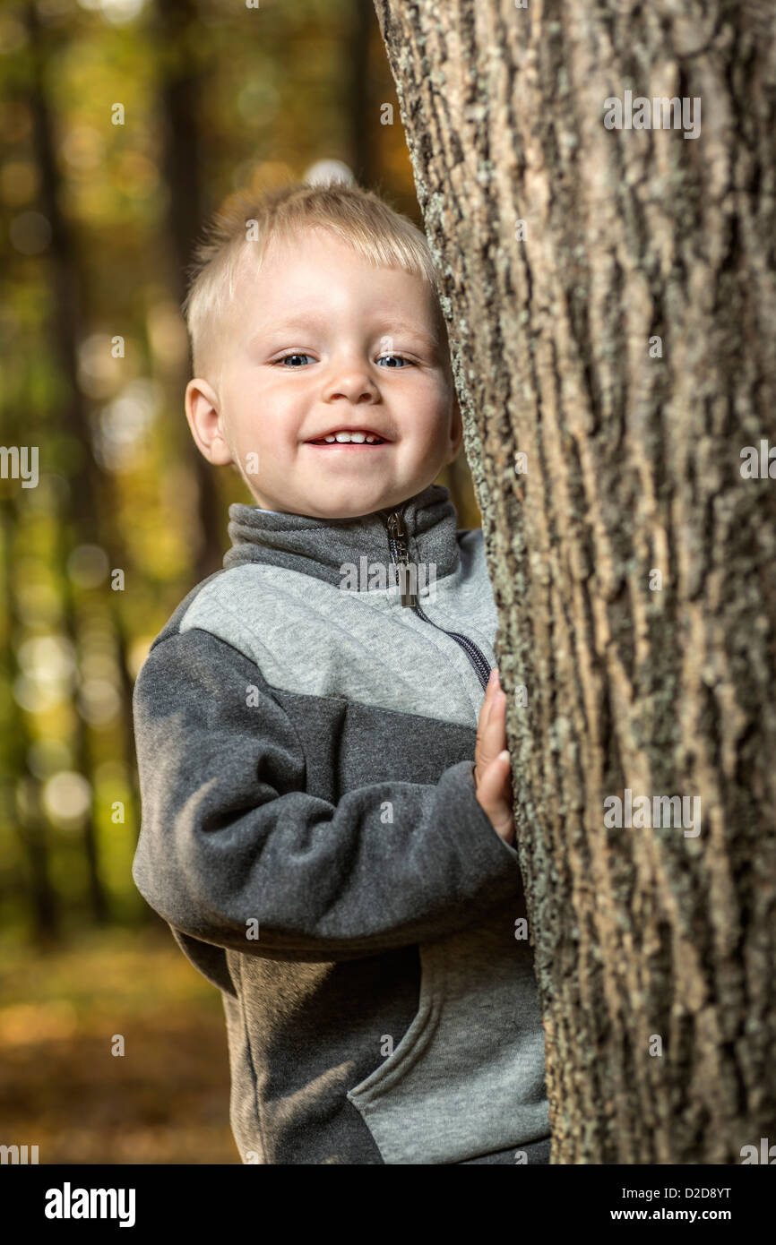 A young boy standing by a tee trunk and smiling happily Stock Photo