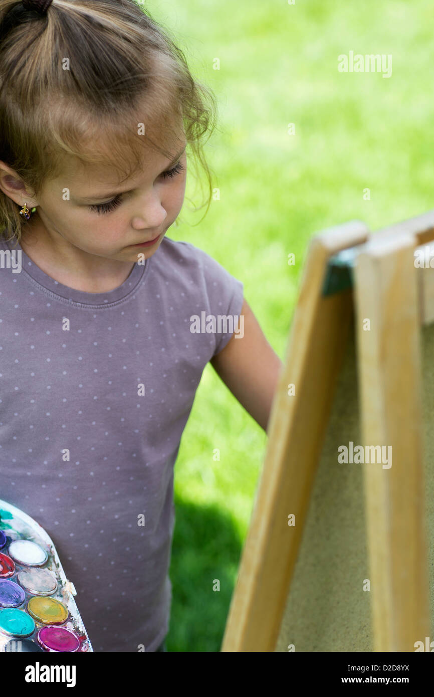 A young girl concentrating seriously while she's painting on an easel Stock Photo