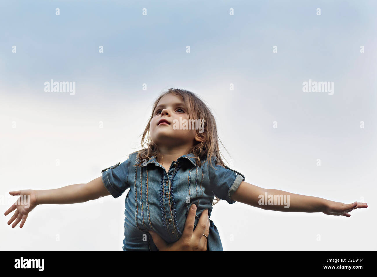 A hand holding up a young girl who is pretending to be an airplane Stock Photo