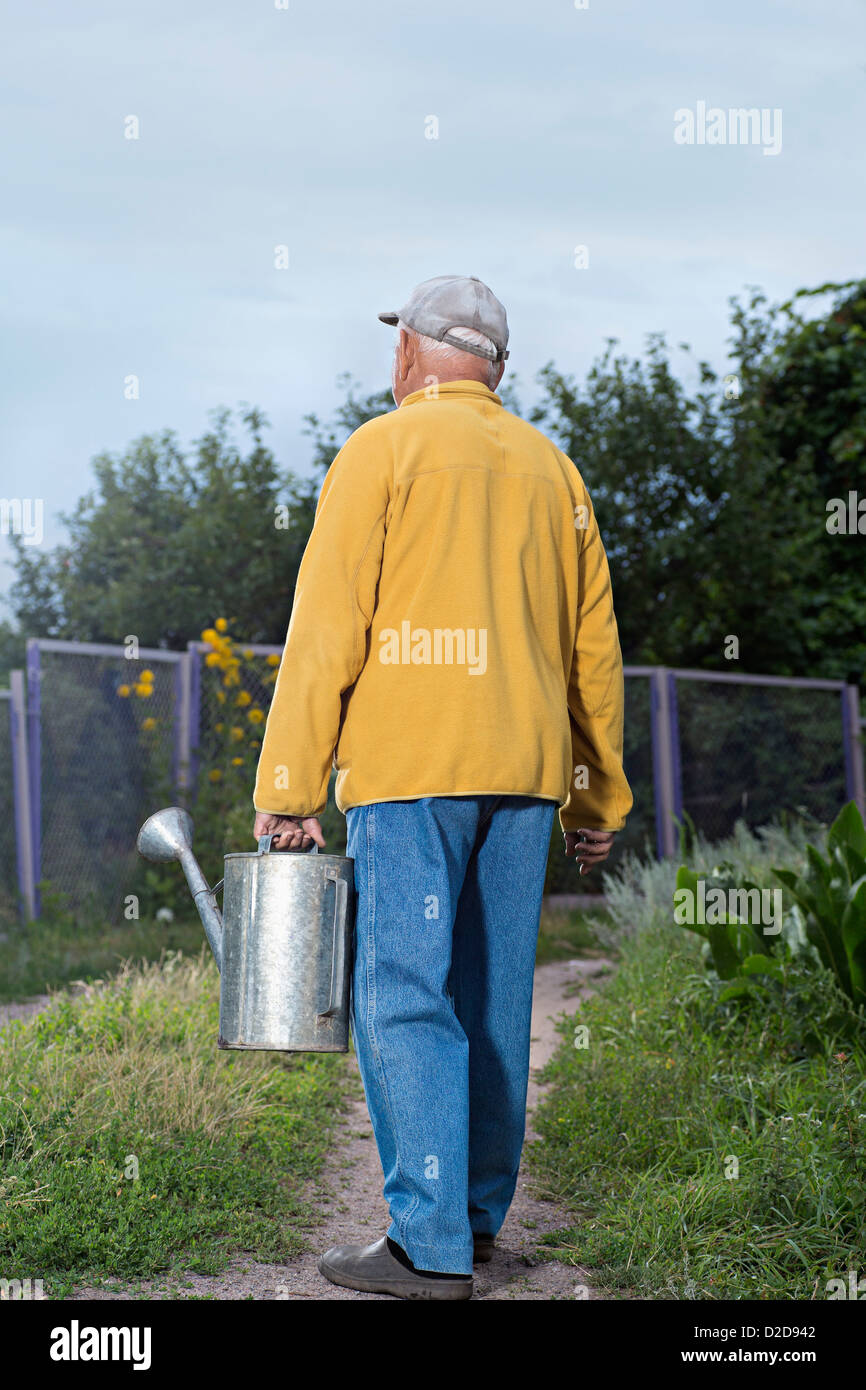 A senior man carrying a metal water can in his backyard Stock Photo