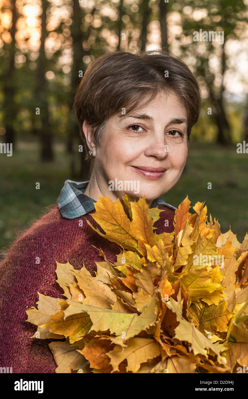 A mature woman holding a bunch of autumn leaves in nature Stock Photo