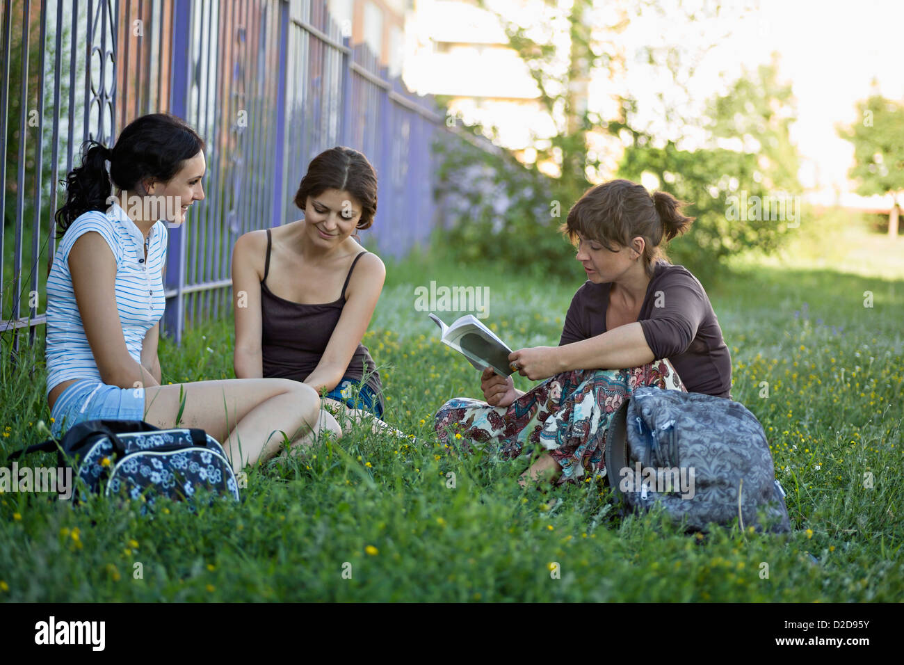 Two friends in a park listening to their friend read from a book Stock Photo