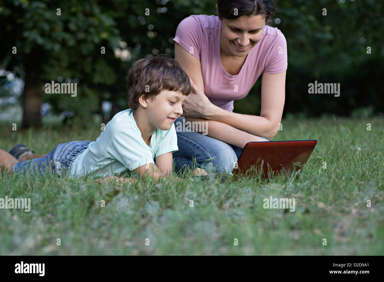 A mother and her son laughing while watching something on a laptop in a park Stock Photo