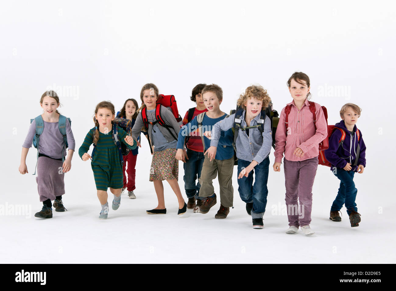 A group of school kids wearing backpacks and running forward Stock