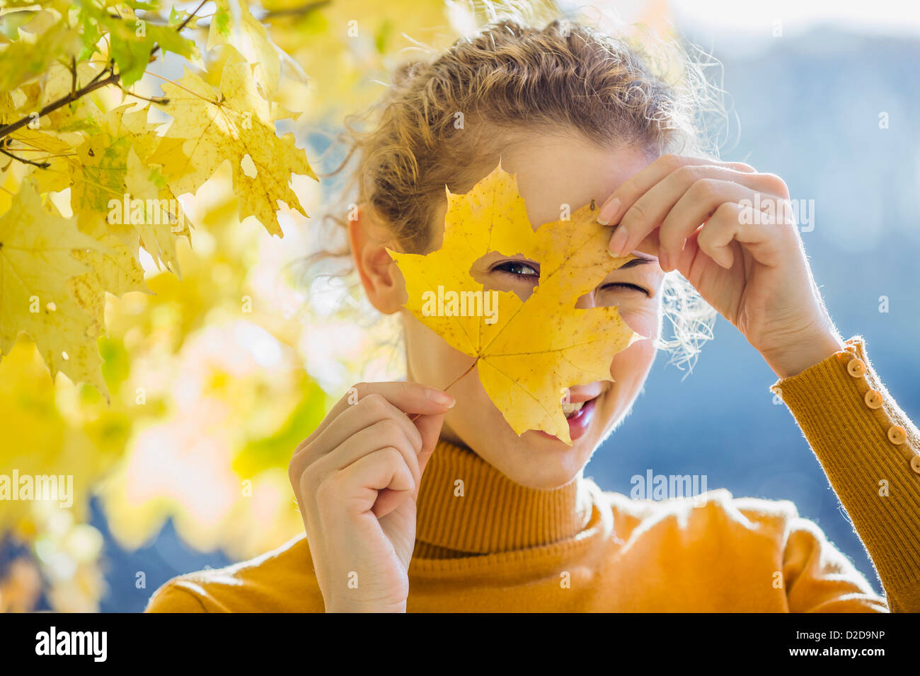 A woman looking through a hole in a leaf she's holding up to her face Stock Photo