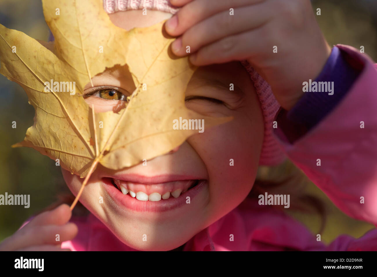 A young girl looking through a hole in a leaf she's holding up to her face Stock Photo