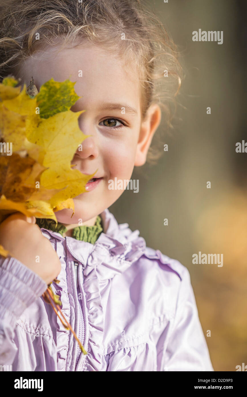 A young girl covering one eye with a bunch of autumn leaves Stock Photo