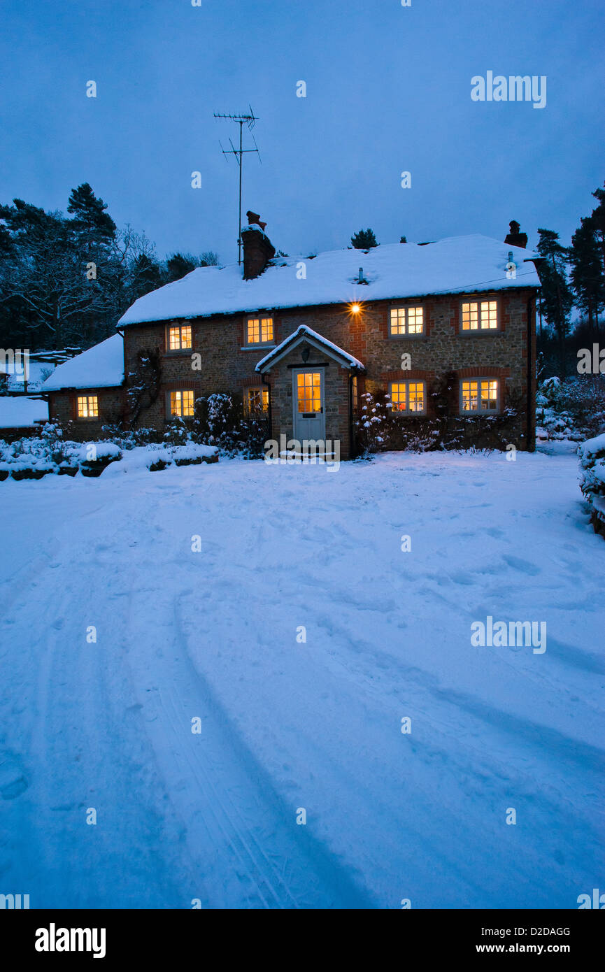 Christmas card image of a snowy cottage at night with all the lights on and tracks in the snow Stock Photo