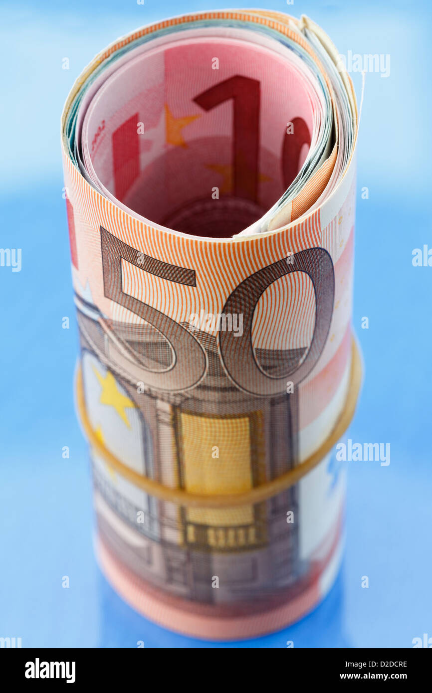 50 Euro note on a Eurozone money roll of Euros rolled up with an elastic band on a blue background Stock Photo