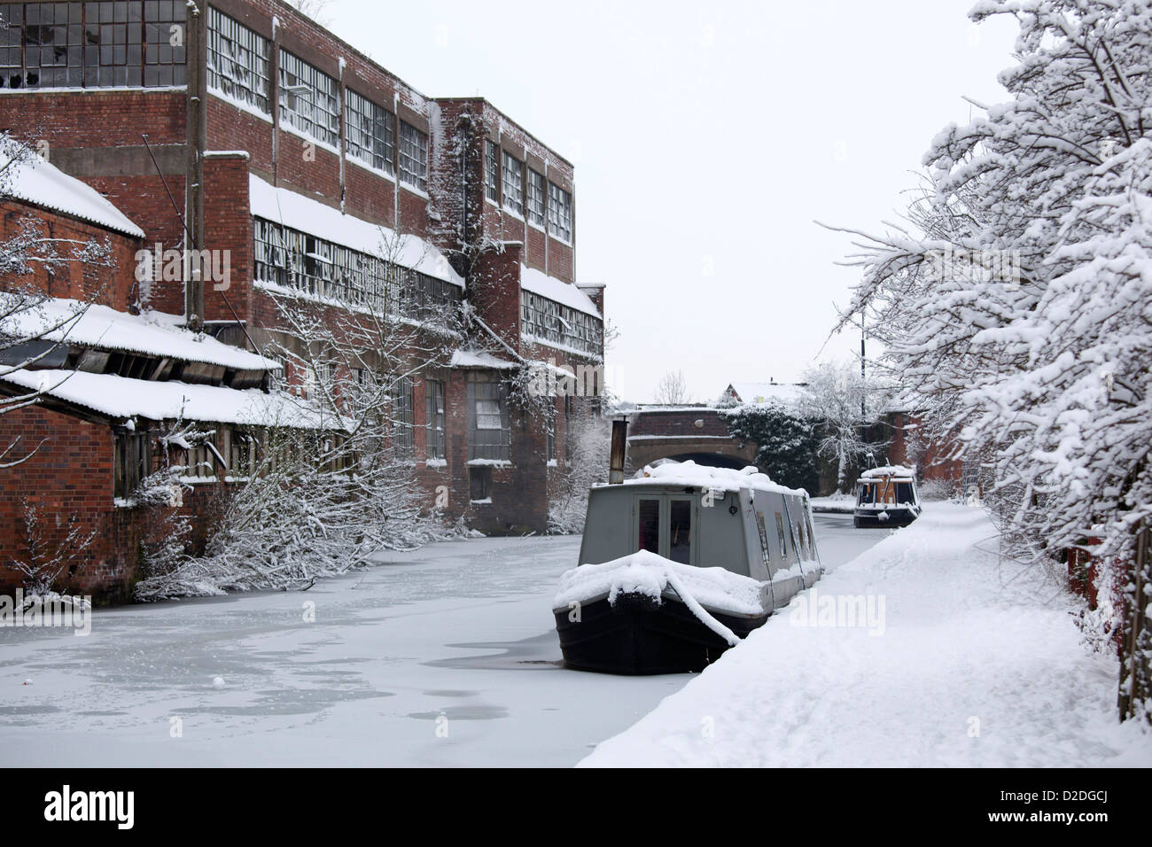 A frozen canal boat sits on the Coventry canal in Atherstone, overshadowed by a unused factory on the Coleshill Road. Stock Photo