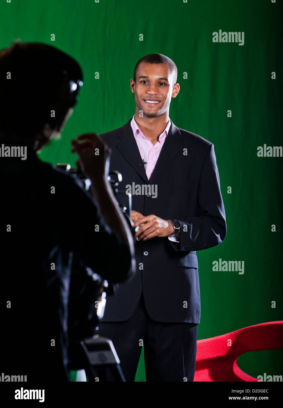 Presenter in a green screen Television studio chats with a camera operator silhouetted in foreground. Stock Photo