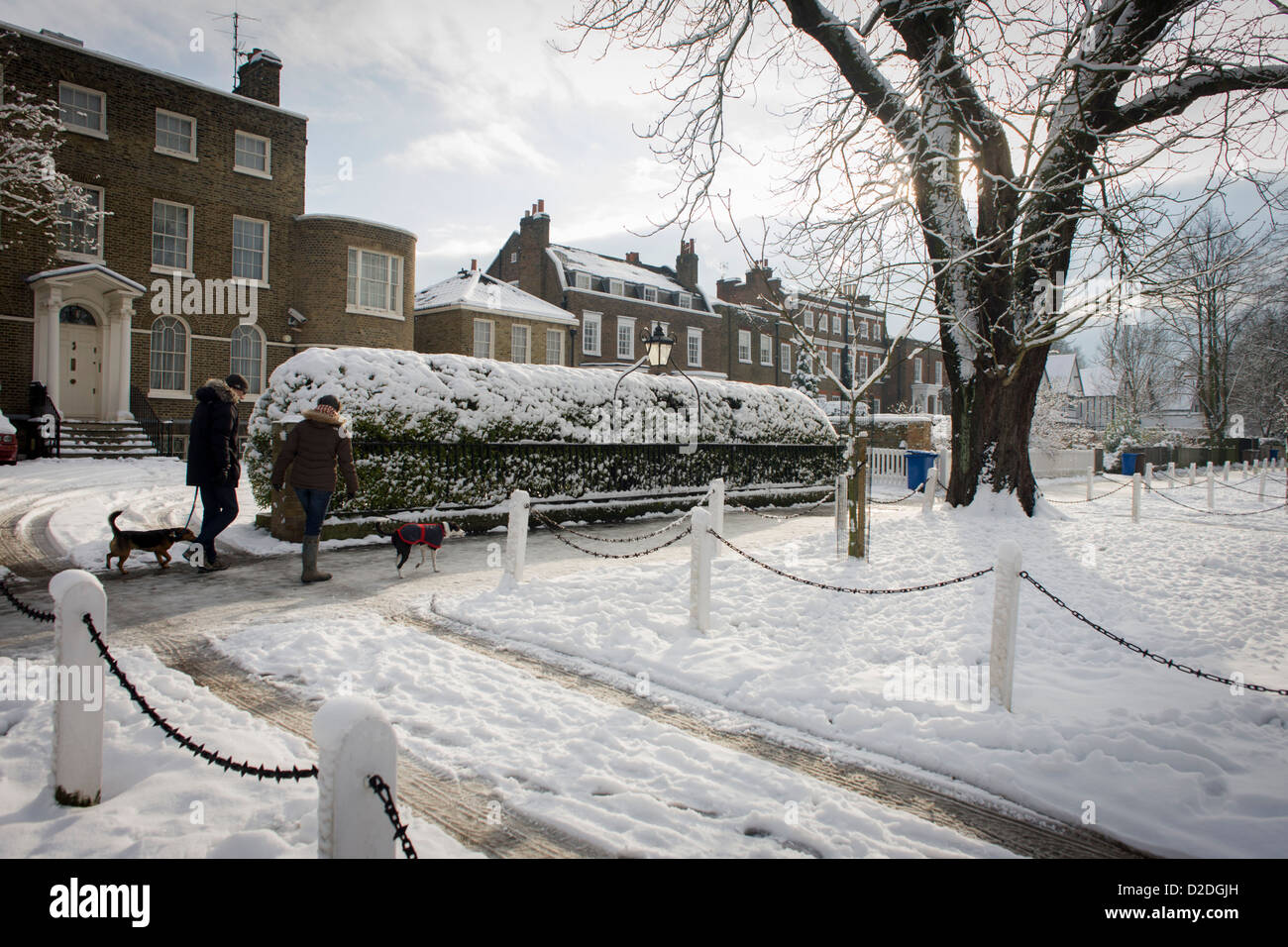 Dog walkers pass-by Dulwich Village homes landscape during mid-winter snow. Stock Photo