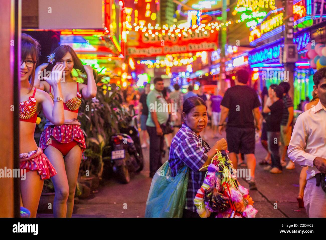 Jan. 12, 2013 - Bangkok, Thailand - A woman who sells garters to workers in the red light district of Soi Cowboy walks down the street between ''Ladyboy'' entertainers and tourists. In Thai, the ladyboys are called kathoey. Many work in the entertainment and night life sectors of the Thai economy.  Prostitution in Thailand is illegal, although in practice it is tolerated and partly regulated. Prostitution is practiced openly throughout the country. The number of prostitutes is difficult to determine, estimates vary widely. Since the Vietnam War, Thailand has gained international notoriety amon Stock Photo