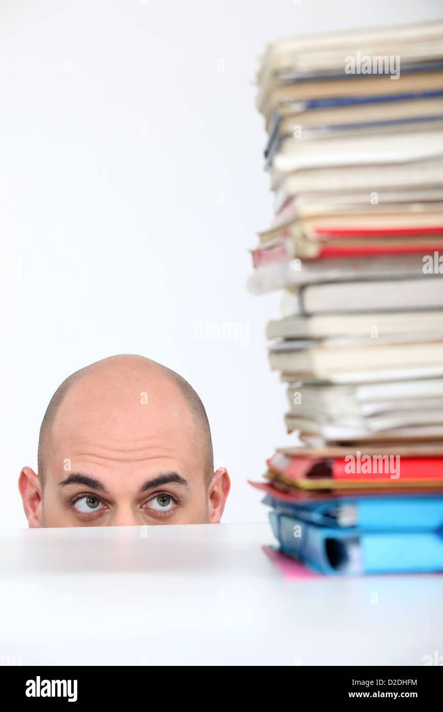 Man hiding behind a desk watching a stack of books Stock Photo