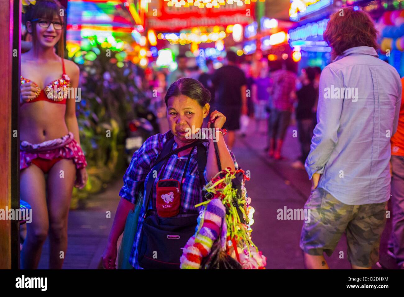 Jan. 12, 2013 - Bangkok, Thailand - A woman who sells garters to workers in the red light district of Soi Cowboy walks down the street between ''Ladyboy'' entertainers and tourists. In Thai, the ladyboys are called kathoey. Many work in the entertainment and night life sectors of the Thai economy.  Prostitution in Thailand is illegal, although in practice it is tolerated and partly regulated. Prostitution is practiced openly throughout the country. The number of prostitutes is difficult to determine, estimates vary widely. Since the Vietnam War, Thailand has gained international notoriety amon Stock Photo