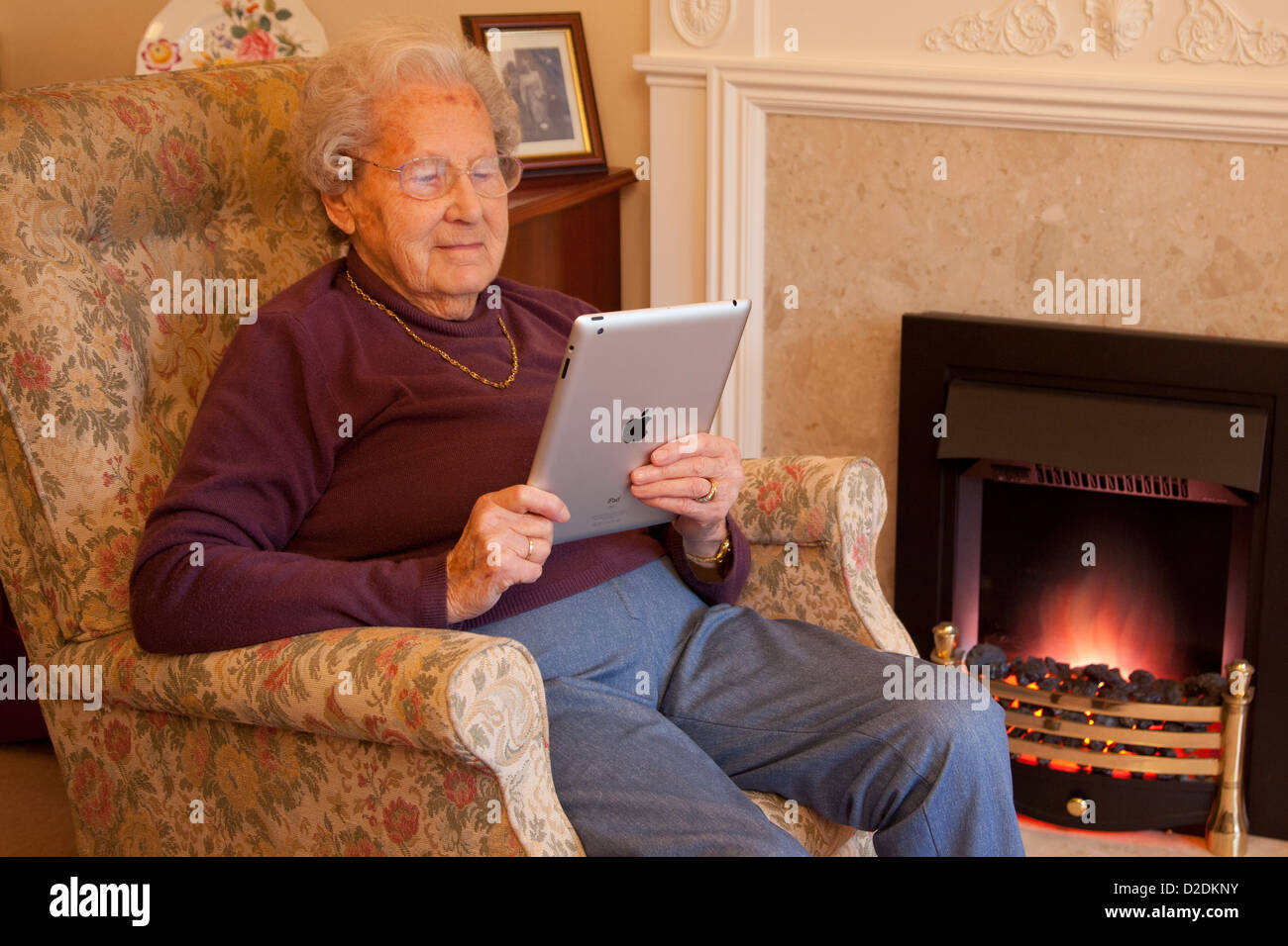 Elderly woman pensioner with glasses relaxing on chair reading her ipad tablet Stock Photo