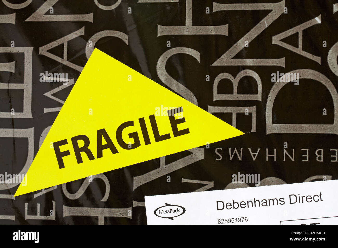 Yellow fragile sticker stuck on Debenhams plastic bag of parcel from Debenhams Direct online order Stock Photo