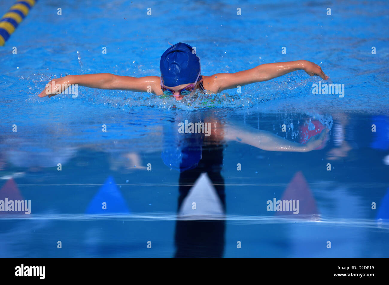 Young swimmer swimming the butterfly in blue water reflecting off the water. Stock Photo