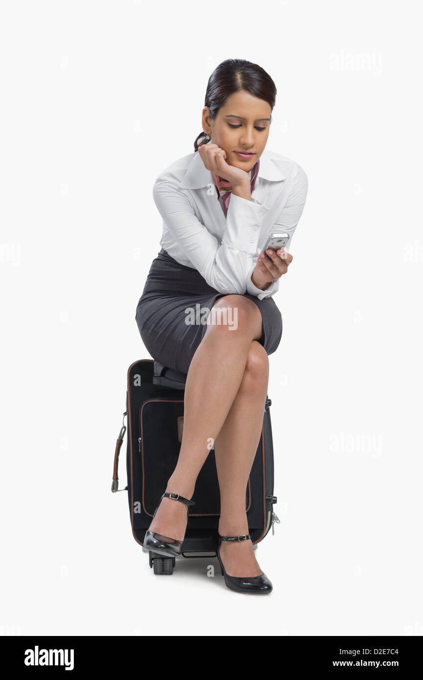 Air hostess sitting on her bag and text messaging on a mobile phone Stock Photo