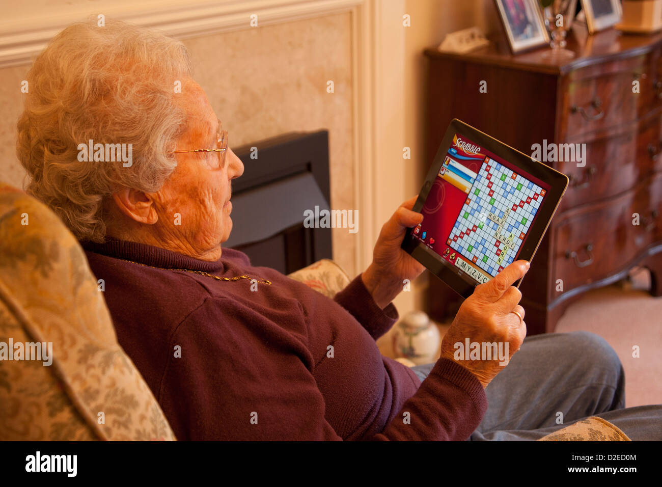 Elderly woman pensioner with glasses on apple ipad tablet at home relaxing on chair playing a