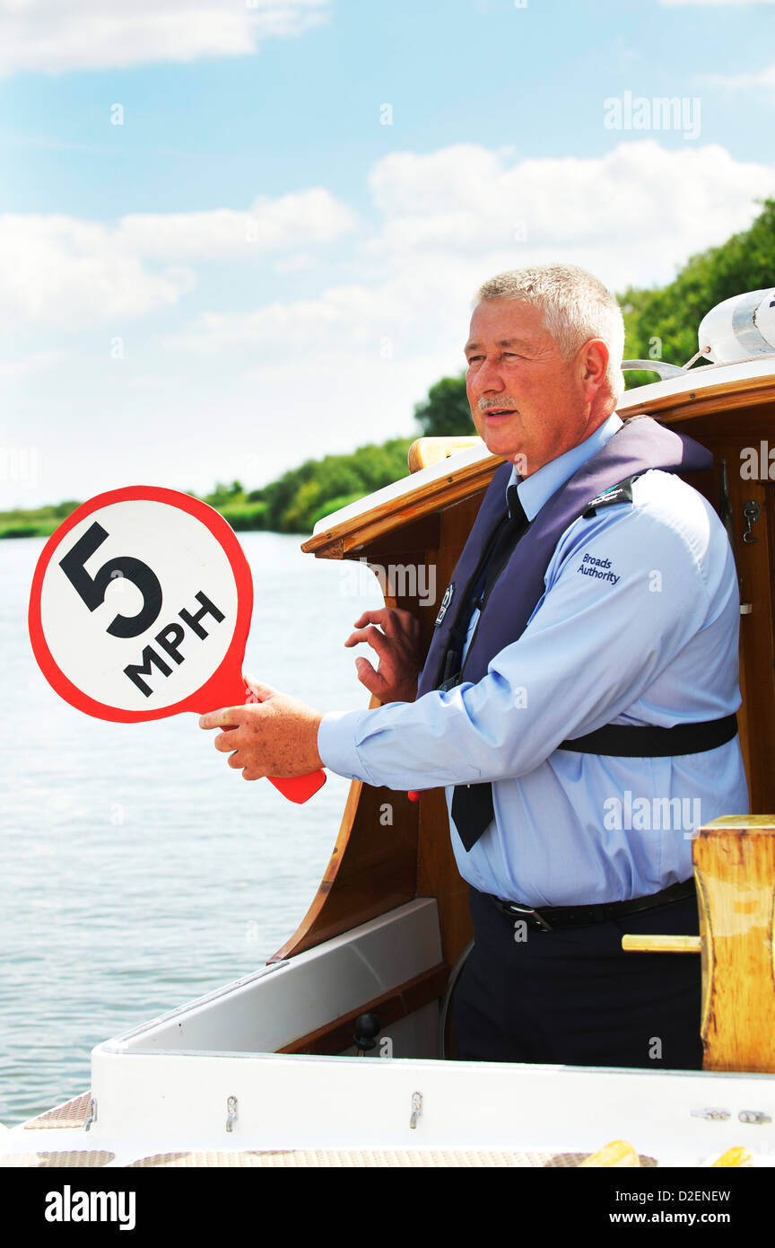National Parks Broads Authority Police Officer holds out speed limit sign for passing holiday makers on the Norfolk Broads Stock Photo