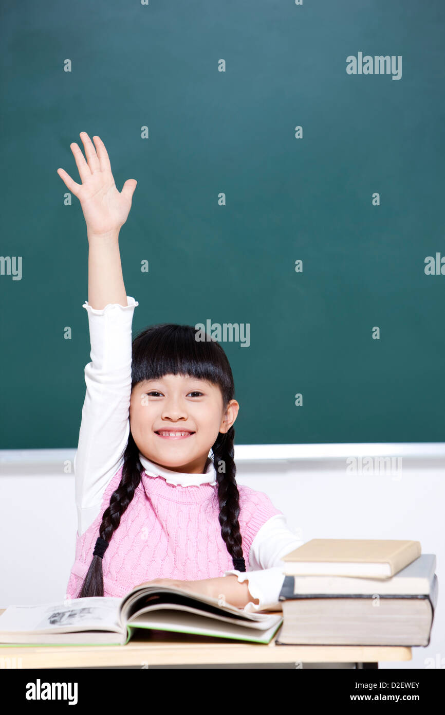 Cheerful schoolgirl raising hand in classroom Stock Photo - Alamy