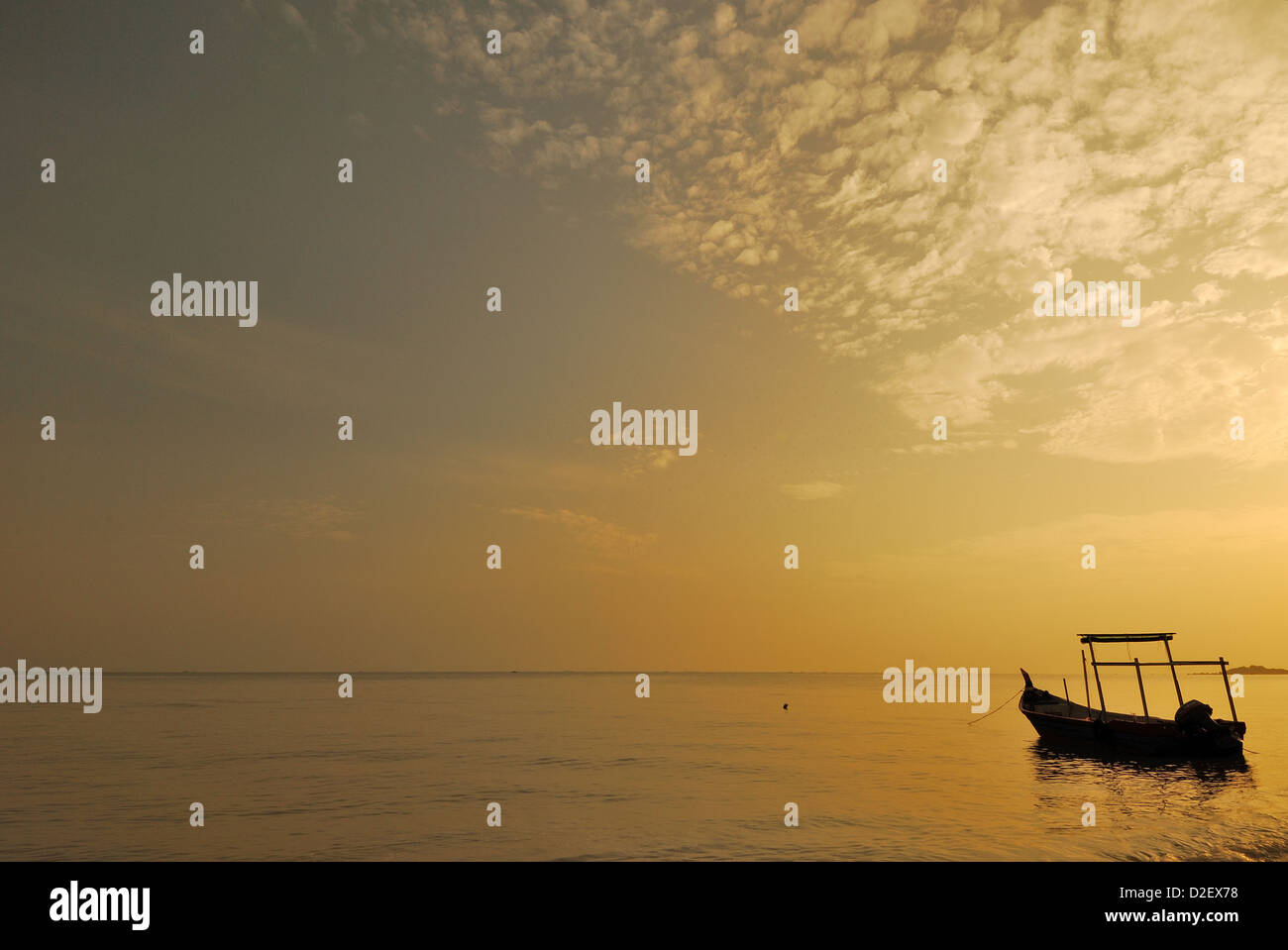 Lonely boat by the seaside during morning sunrise with golden color setting horizon, Penang, Malaysia. Stock Photo