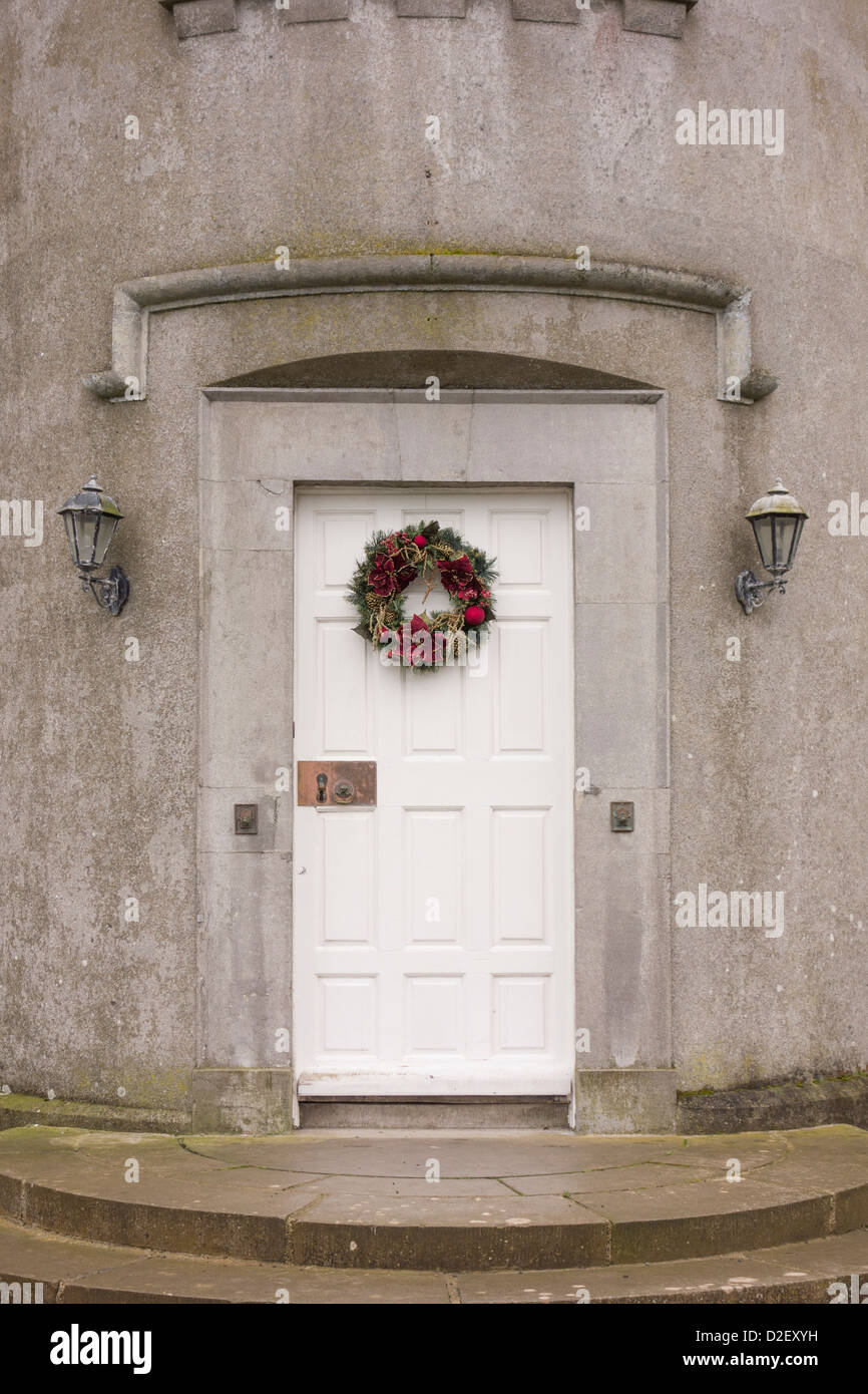 A traditional Christmas wreath hanging on a white house door. Stock Photo