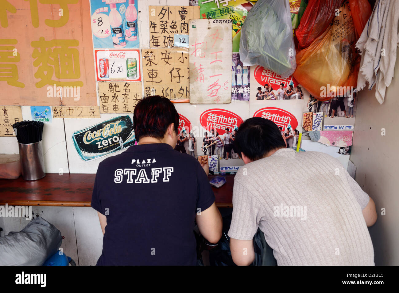 Hong Kong, China, two men sit hunched eat a snack and Stock Photo