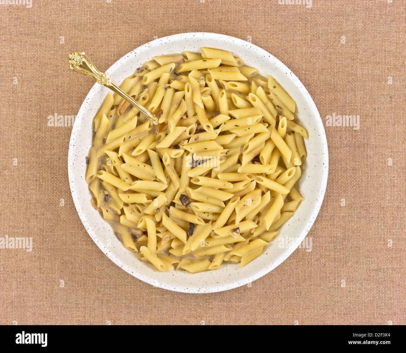 Large serving of penne Italian pasta with gold spoon on a tan cloth background. Stock Photo