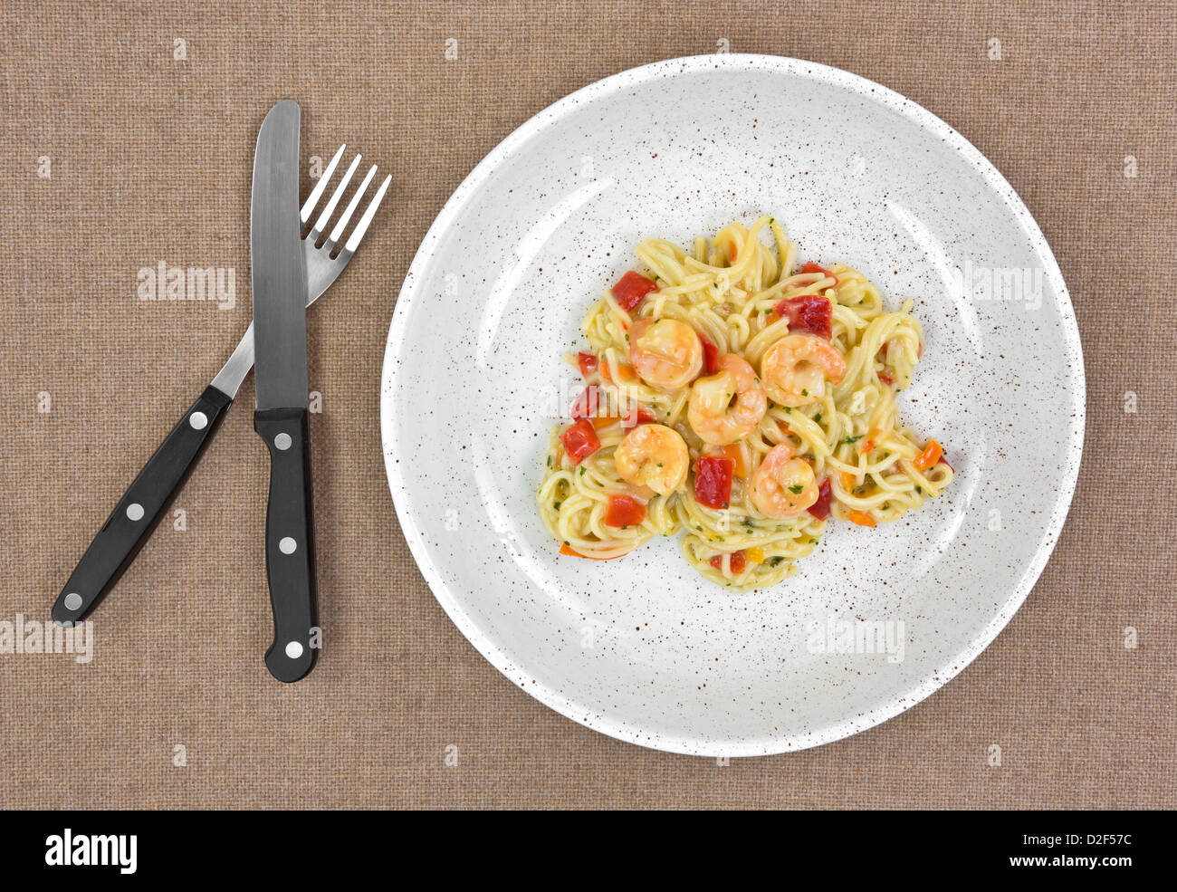 A small serving of angel hair pasta with shrimp and vegetables on cloth background with fork and knife. Stock Photo