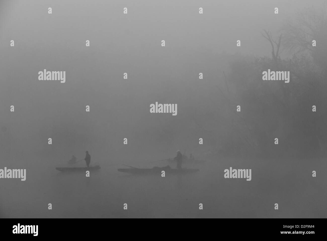 Silhouette Of People Rowing Boat - Shore of an oxbow (backwater) of Tisza river in black and white at sunrise with fishermen Stock Photo