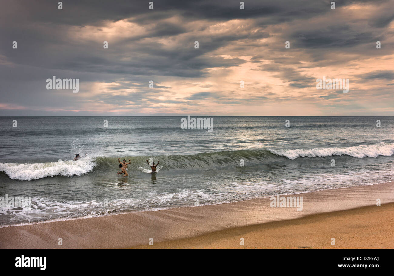 Swimmers take a late dip in the Arabian Sea at Thottada beach, Kannur, Kerala, India. it is dusk and the sun has set. Stock Photo