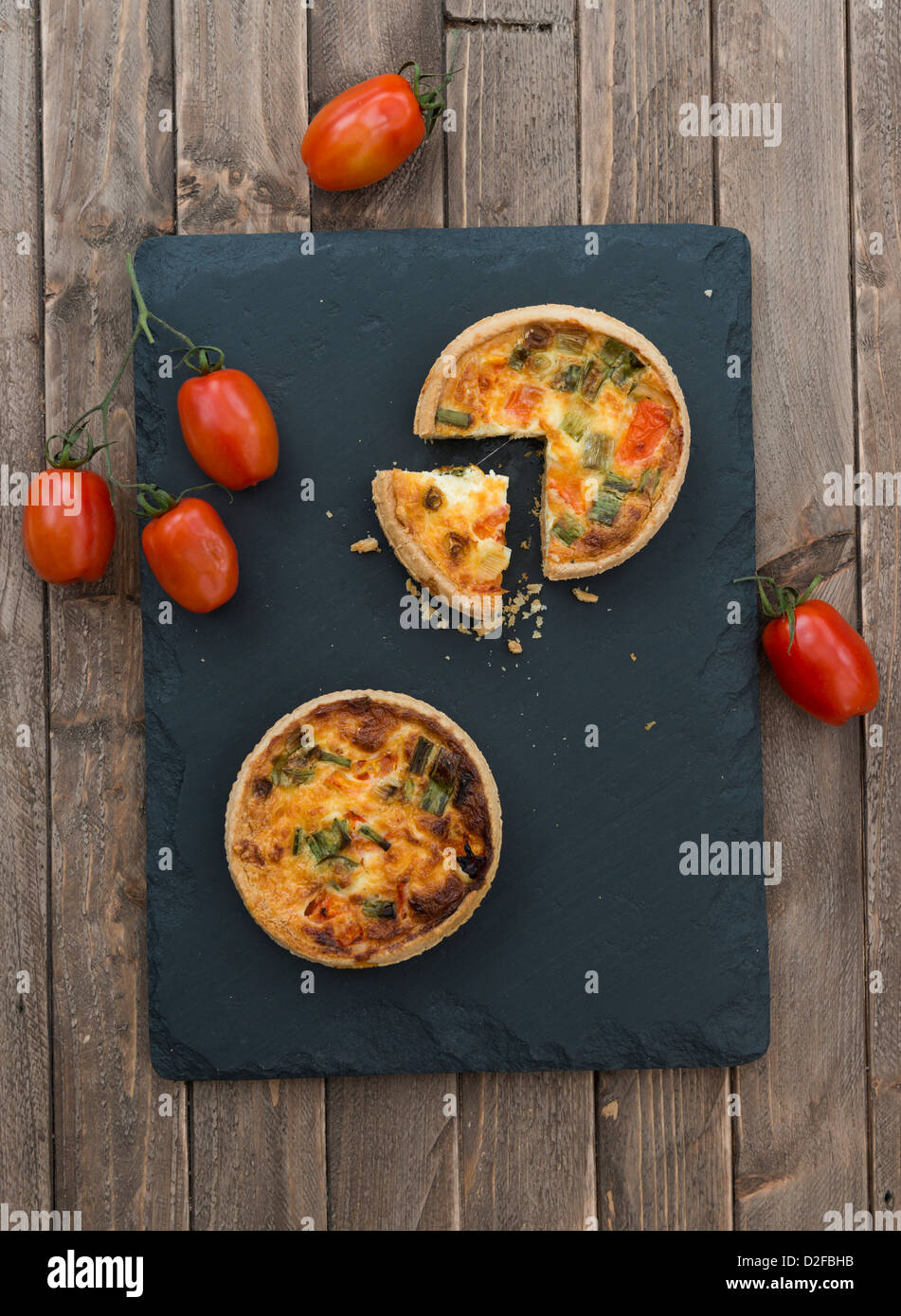 Cooked cheese, spring onion and tomato quiche, on a slate board, garnished with tomatoes. Stock Photo