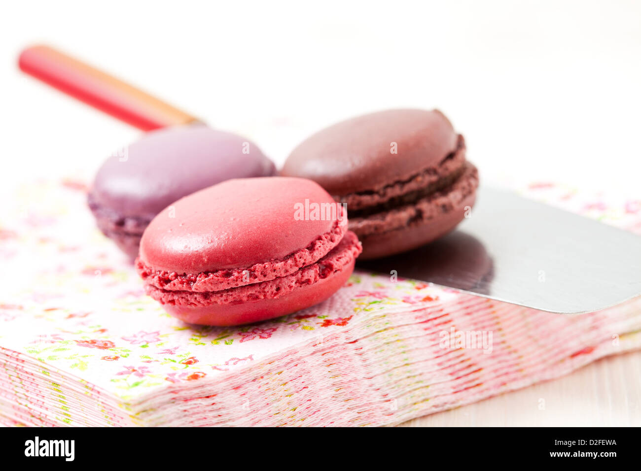 Close-up of three colorful macaroons on serviette and cake server on light background Stock Photo
