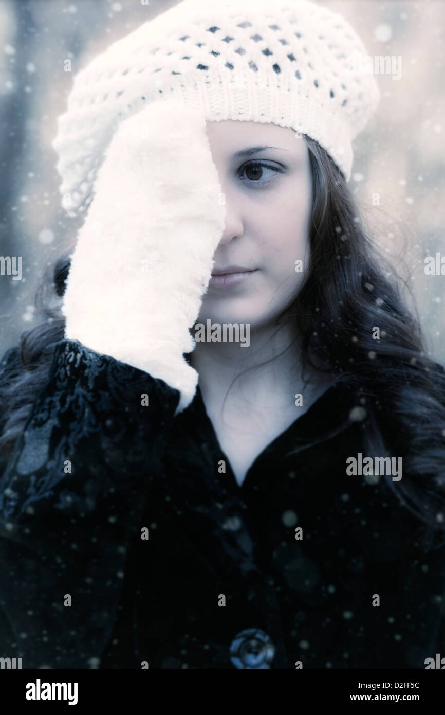 a woman in a black coat with a white cap is holding a gloved hand in front of one of her eyes Stock Photo