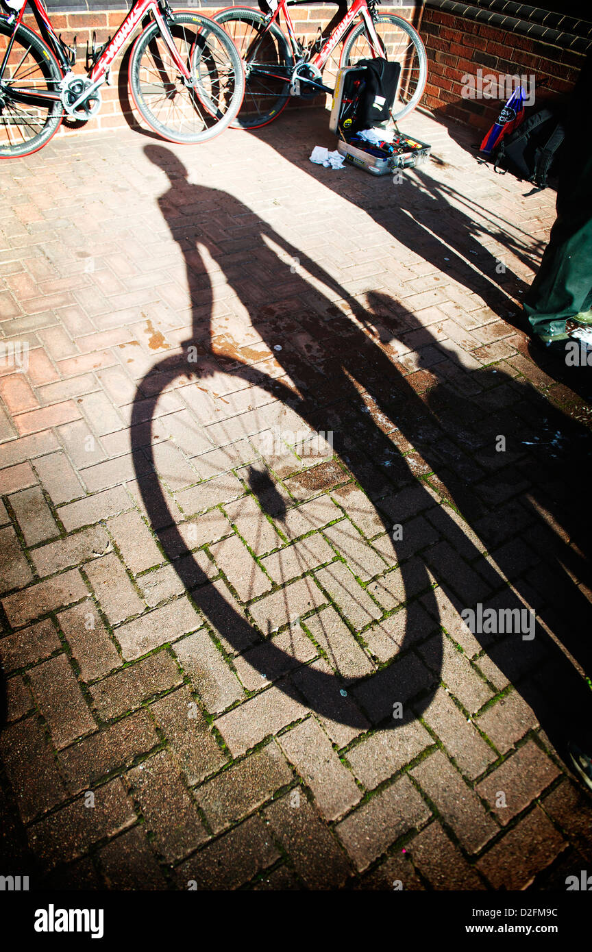 Cleaning bikes... a bike mechanic at the Tour of Britain cleans the team bikes and hold a wheel to create a silhouette Stock Photo