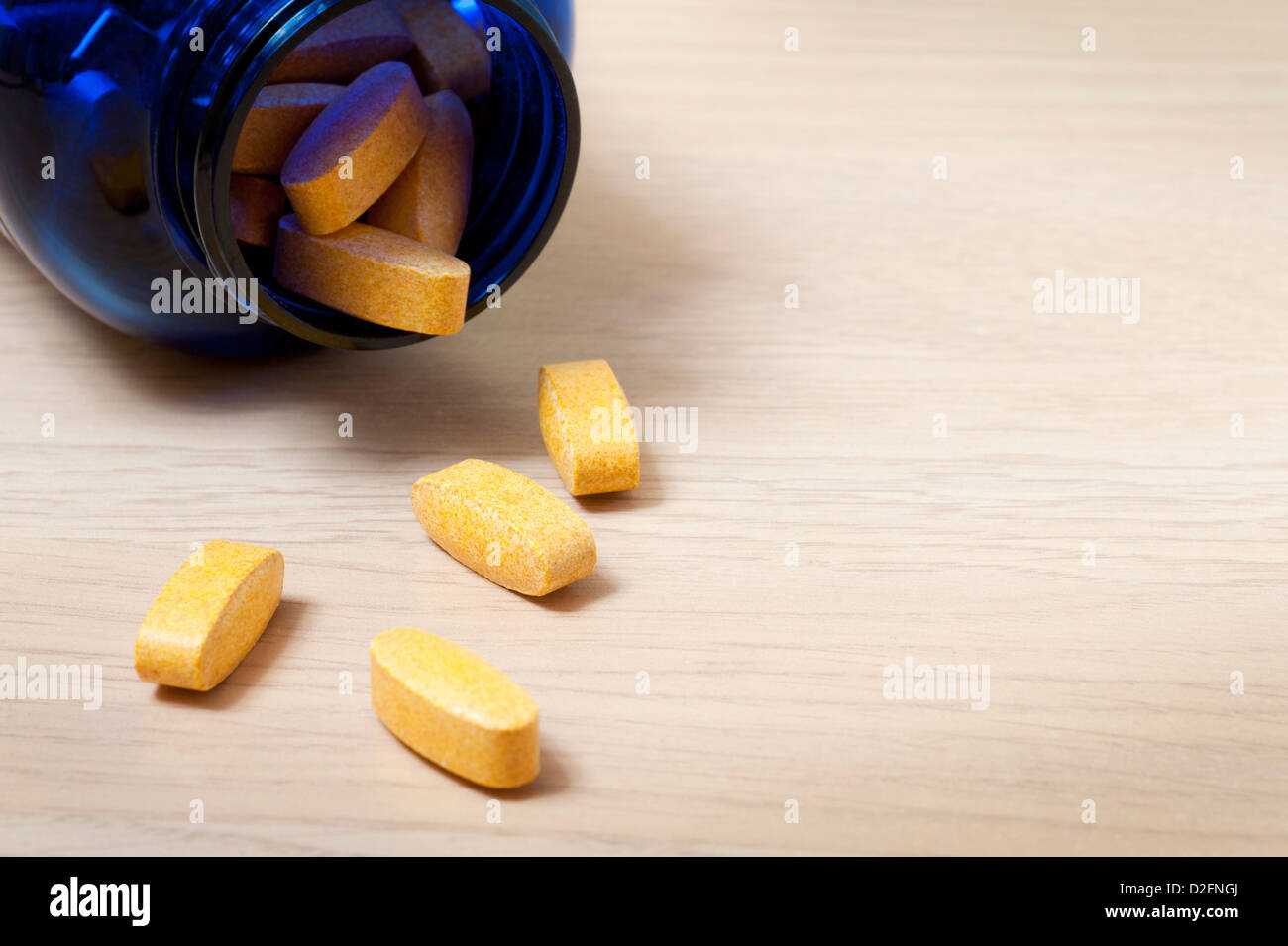Blue bottle of yellow vitamin pills with some spilling out onto the table Stock Photo