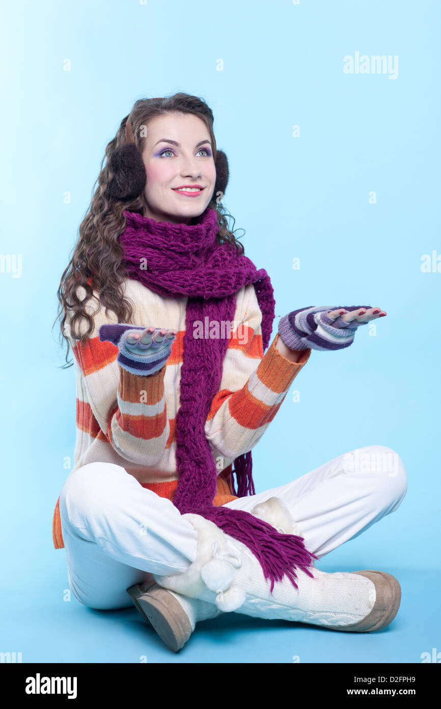 Young pretty woman in winter dress sitting on blue background Stock Photo