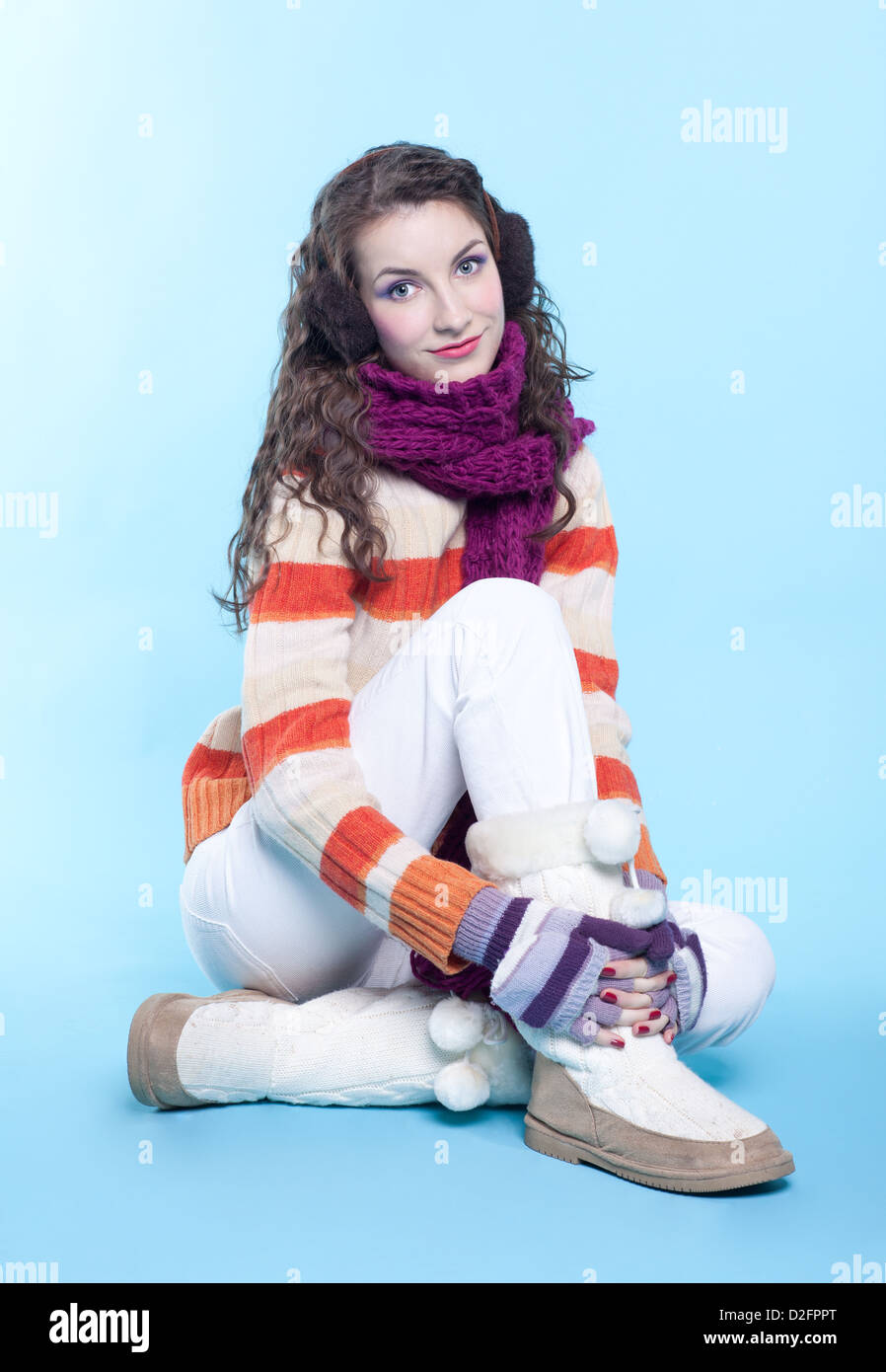 Young pretty woman in winter dress sitting on blue background Stock Photo